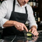 Barman professionnel découpant un citron vert frais sur un comptoir en marbre noir dans un bar premium